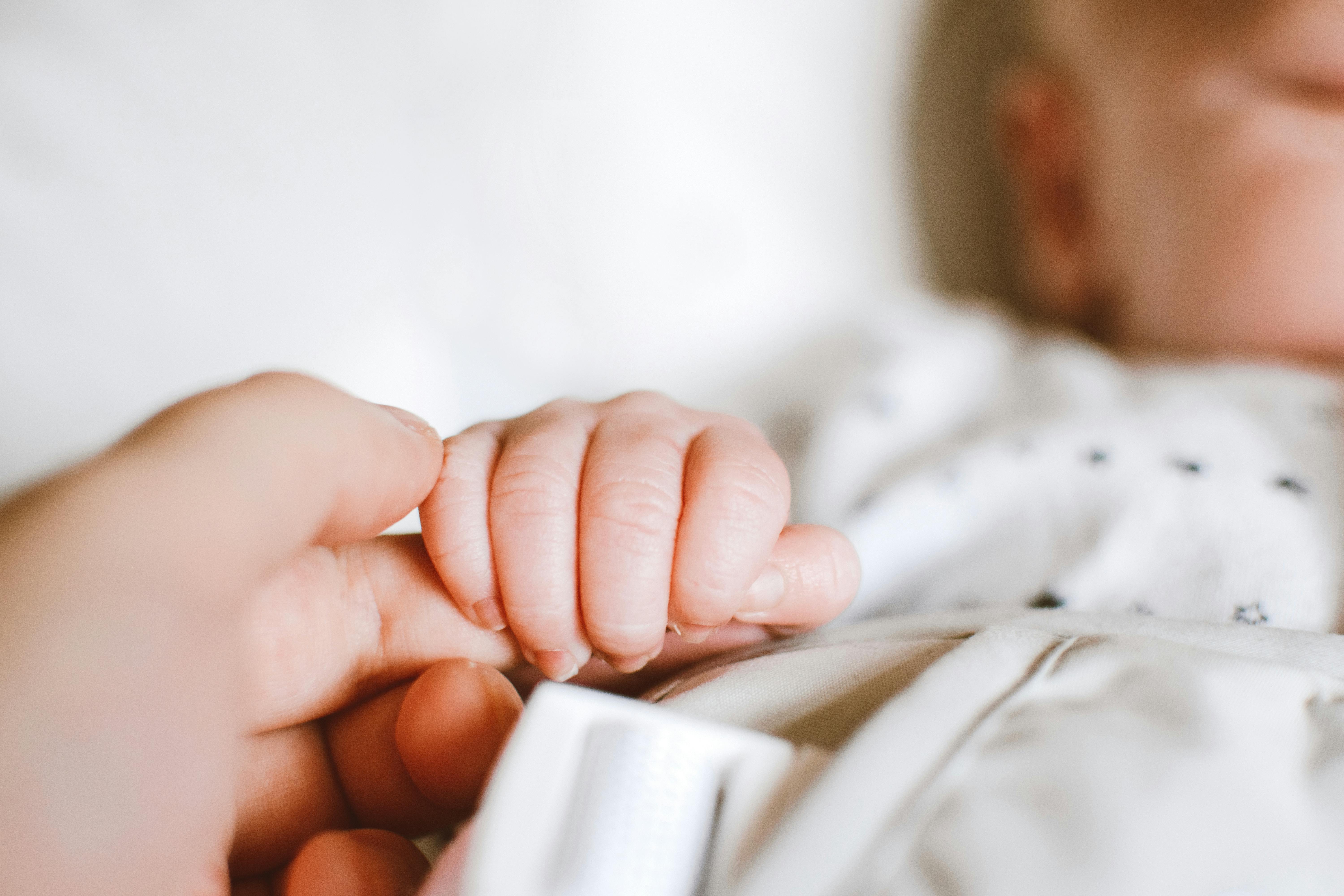 A newborn baby holding an adult’s finger